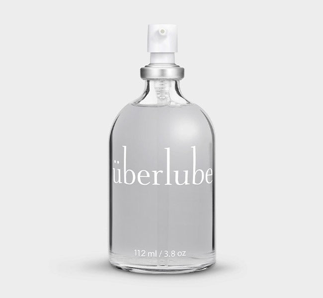 A clear glass bottle with a white spray nozzle, labeled 'Uberlube' and marked with a volume of 112 ml / 3.8 oz. — 1