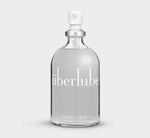 A clear glass bottle with a white spray nozzle, labeled 'Uberlube' and marked with a volume of 112 ml / 3.8 oz. — 1
