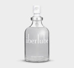 A clear glass bottle with a white spray nozzle, labeled 'Uberlube' and marked with a volume of 55 ml / 1.86 oz. — 10