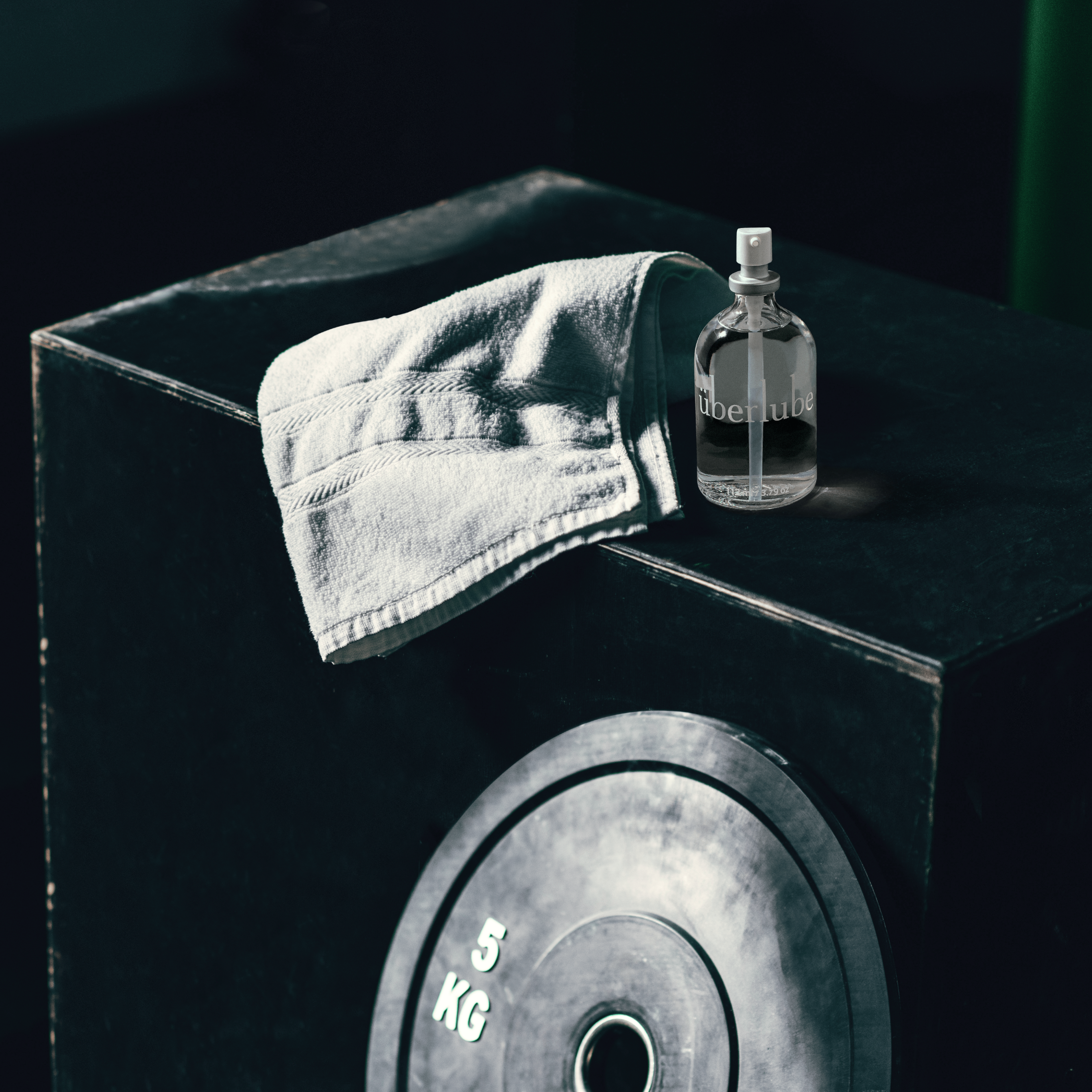 Black box with a 5K weight leaning. a towel and a glass bottle of uberlube on top of the box. Black background.