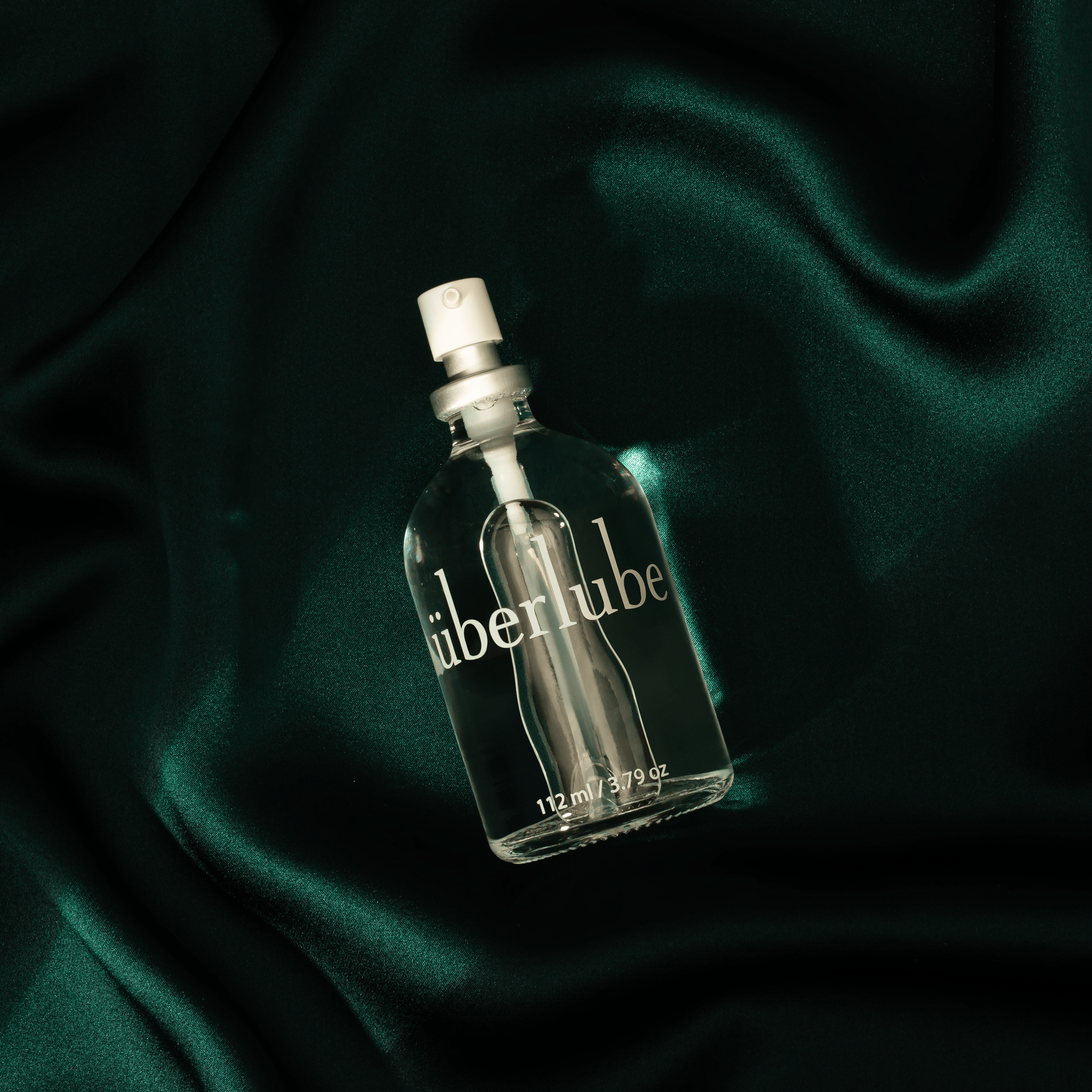 Glass uberlube bottle on green silk background